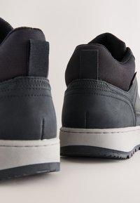 Ansicht von hinten auf schwarze und graue Sportschuhe mit weißen Sohlen vor neutralem Hintergrund.