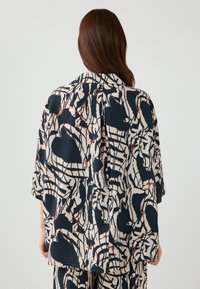 Top leggero in tessuto blu navy con motivi astratti in crema e rosso. Presenta una vestibilità rilassata e maniche corte, progettato per il comfort.