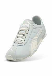Ανοιχτό γκρι αθλητικό παπούτσι Puma με λευκές ρίγες και κορδόνια, που δείχνει μια υφασμένη λαστιχένια σόλα και ραμμένες λεπτομέρειες.