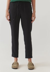 Schwarze Jogginghosen mit einem Kordelzugbund, Seitentaschen und schmaler Passform. Der Stoff ist weich und die Bündchen sind leicht hochgekrempelt.