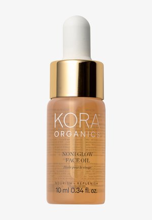 L'huile pour le visage Noni Glow de KORA Organics dans un flacon en verre transparent avec un capuchon doré et un compte-gouttes, contient un liquide ambre avec une étiquette blanche.