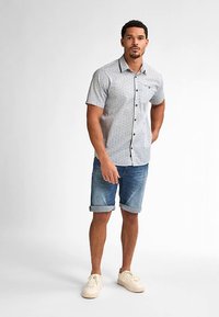 Košile s krátkým rukávem na knoflíky v světle šedé barvě s puntíkovaným vzorem, doplněná o modré džínové šortky s vyhrnutými nohavicemi a světlé tenisky.