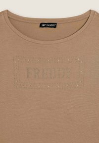 Camiseta beige de tela suave con escote redondo y un logo decorativo "FREDDY" adornado con piedras brillantes en la parte frontal.
