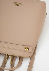 Beżowa skórzana torebka z złotymi elementami, z zamknięciem na zamek błyskawiczny, dwoma suwakami i fakturowaną powierzchnią. Logo wyeksponowane w widocznym miejscu.