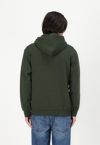 Grønn hettegenser laget av mykt materiale, med lange ermer og kengurulomme. Brukt med blå jeans, sett fra bak.