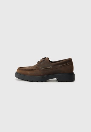 Braune Lederschuhe mit abgerundetem Zehenbereich, dicker schwarzer Gummisohle und Ösen-Schnürung. Mit dezenten Nähten und seitlichen Ösen.