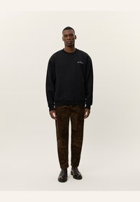 Hanorac negru cu guler rotund și logo brodat, combinat cu pantaloni maro cu modele variate și botine negre.