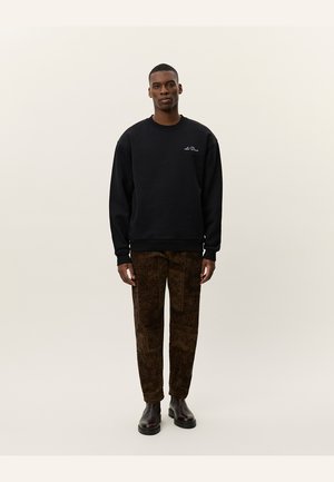 Svart hettegenser med rund hals og brodert logo, kombinert med mønstrede brune bukser med varierte design og mørke støvler.