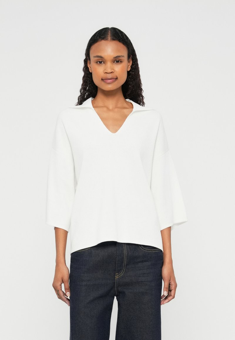 Sweater branco de malha com decote em V e colarinho, apresentando mangas de três quartos e um corte descontraído. Combinado com jeans de denim escuro.