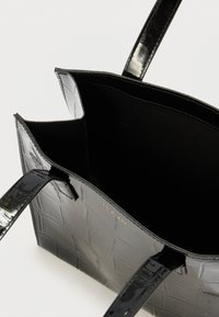 Svart veske i imitert lær med krokodillemønster; har to lange håndtak og et romslig interiør med svart tekstilfôr.