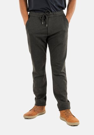 Pantalones jogger de color gris carbón con cintura ajustable, piernas estilizadas, bolsillos laterales y una textura suave. Llevados con zapatos marrones de cordones.