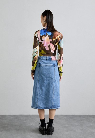 Μακρυμάνικη, διαφανής μπλούζα με λουλούδια σε καφέ απόχρωση, με πολύχρωμα λουλουδάτα μοτίβα. Συνδυάζεται με μια μπλέ τζιν μίντι φούστα και μαύρα παπούτσια με κορδόνια.