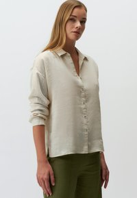 Lichtbeige button-up overhemd gemaakt van textiel, met een kraag, opgerolde mouwen en een rechte zoom. Gecombineerd met olijfgroene broek.
