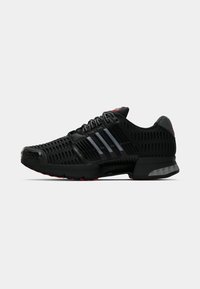 Baskets de sport noires avec un design perforé, dotées de trois rayures grises, d'accents rouges et d'une semelle texturée pour l'adhérence et la stabilité.