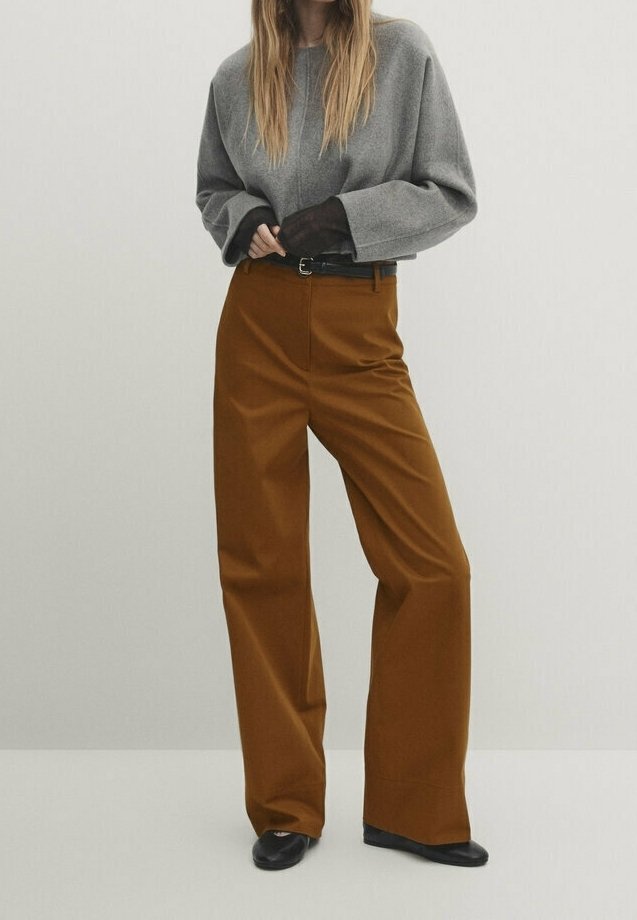 Grijze oversized trui met verlaagde schouders, gecombineerd met hoog-waist bruine wijde broek en zwarte platte schoenen. Eenvoudig, minimalistisch ontwerp.