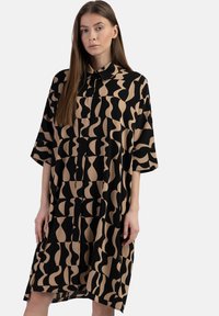 Hemdblusenkleid in Schwarz und Beige mit abstraktem Muster. Mit einem Kragen und kurzen Ärmeln, aus leichtem Stoff gefertigt.