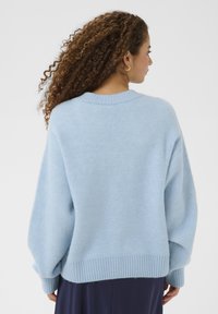 Pull surdimensionné bleu clair en tissu doux avec ourlet et poignets côtelés. Présente un col rond et des épaules tombantes.