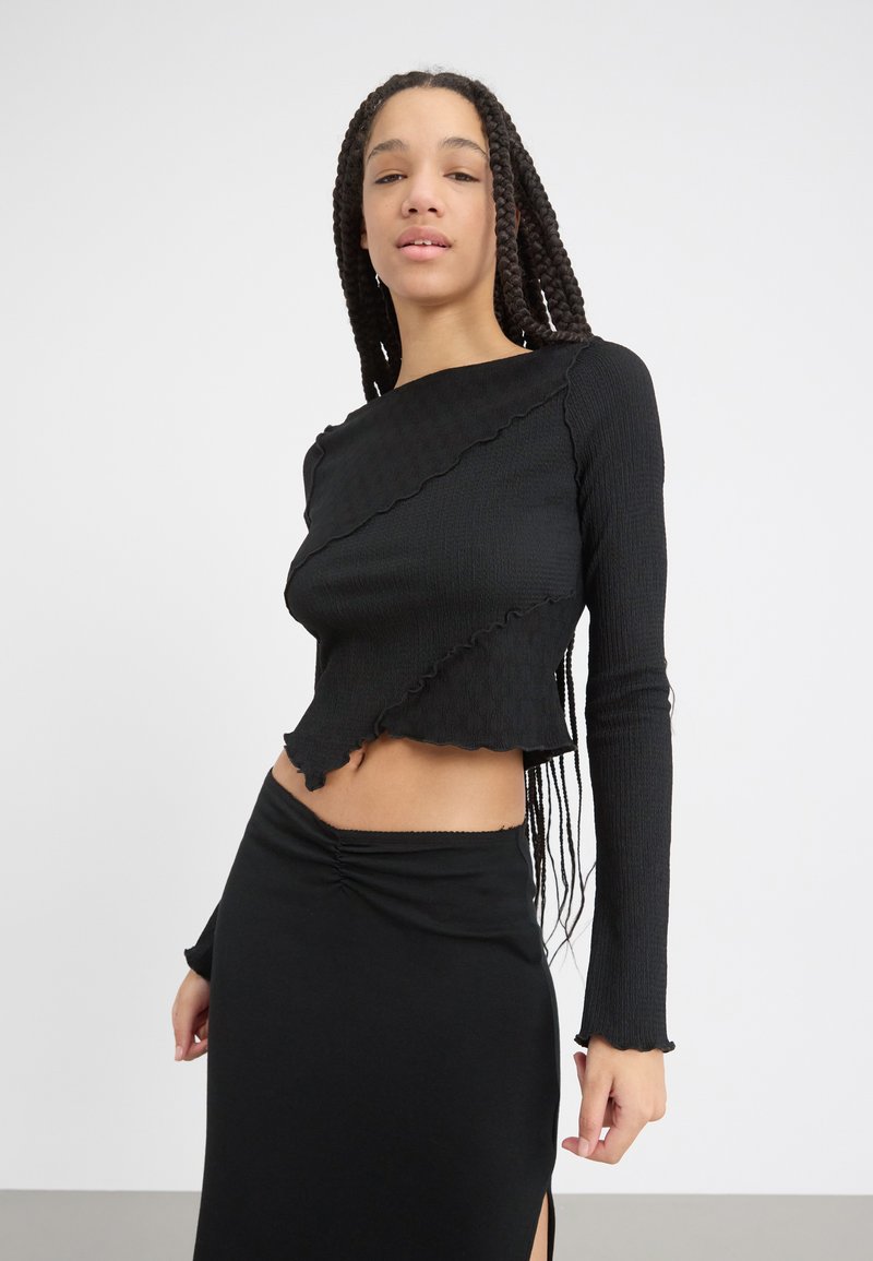 Black cropped long-sleeve top with textured fabric, irregular hem, and ruffled edges, paired with a matching fitted black skirt.