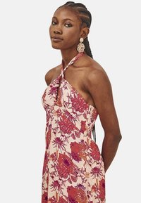 Vestido floral de tirantes en rosa con patrones en rojo y púrpura, con un bodice ajustado y una falda fluida. Textura y caída de tela notables.