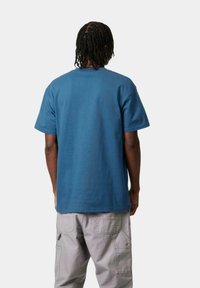 Camiseta azul de algodón con un corte relajado y mangas cortas, vista desde la parte de atrás. Combinada con pantalones cargo de color gris claro. Diseño sencillo, sin patrones.