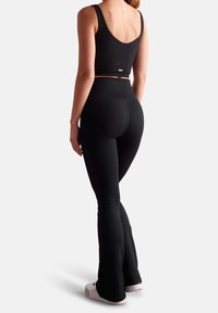 Conjunto deportivo negro de canalé que incluye un top corto y leggings de cintura alta con corte acampanado. El material proporciona una textura ajustada con elasticidad.