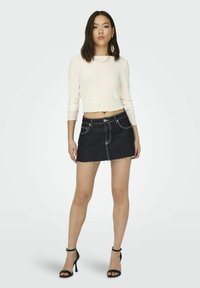 Biely rebrovaný crop top s vlnitými okrajmi, skombinovaný s tmavými džínsovými minisukňami s franémi okrajmi a kontrastným prešívaním. Čierne sandále na opätku.