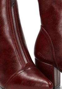 Botas de tobillo de cuero burdeos con puntera afilada, cremallera lateral y tacón de bloque; cuentan con marca grabada y textura suave.