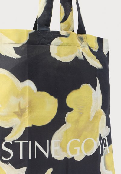 Mustast kangast kandekott kollaste lillemustritega, alumises osas valge tekst "STINE GOYA". Tugevad sangad lihtsaks kandmiseks.