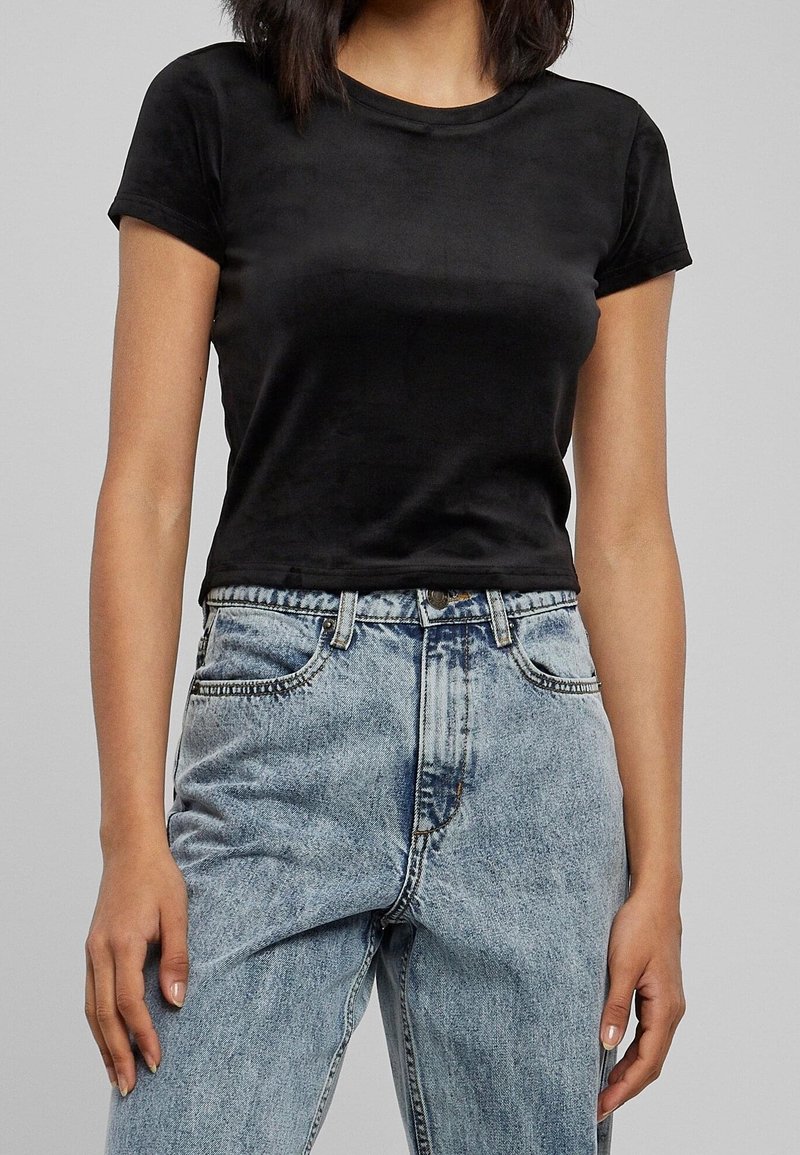 Femme portant un crop top noir uni à manches courtes associé à un jean taille haute en denim bleu clair.