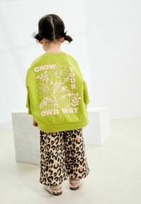Zielony sweatshirt z wytłoczonym kwiatowym wzorem i napisem "GROW YOUR OWN WAY"; w komplecie z szerokimi spodniami w panterkę. Widoczności detali casualowego stroju.