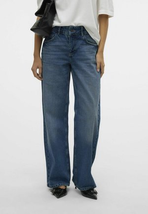 Wijde blauwe spijkerbroeken met een vervaagde afwerking, hoge taille en riemlussen, gecombineerd met puntige zwarte hakken en een zwarte tas.