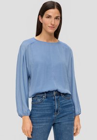 Hellbluse mit lockerer Passform und langen Puffärmeln, Rundhalsausschnitt und einer weichen, glatten Textur, kombiniert mit dunkelblauen Jeans.