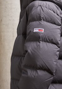 Černá prošívaná bunda s prošíváním, se zipem a malou nášivkou s logem značky na rukávu v červené, bílé a modré barvě.