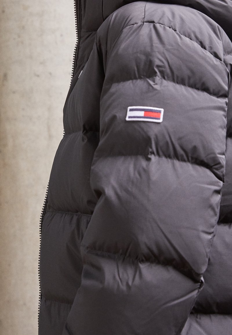 Černá prošívaná bunda s prošíváním, se zipem a malou nášivkou s logem značky na rukávu v červené, bílé a modré barvě.