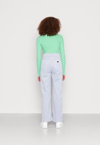 Långärmad mintgrön topp med figurnära passform, tillsammans med ljusblå vida byxor. Vita sneakers och en liten svart emblem på bakfickan.