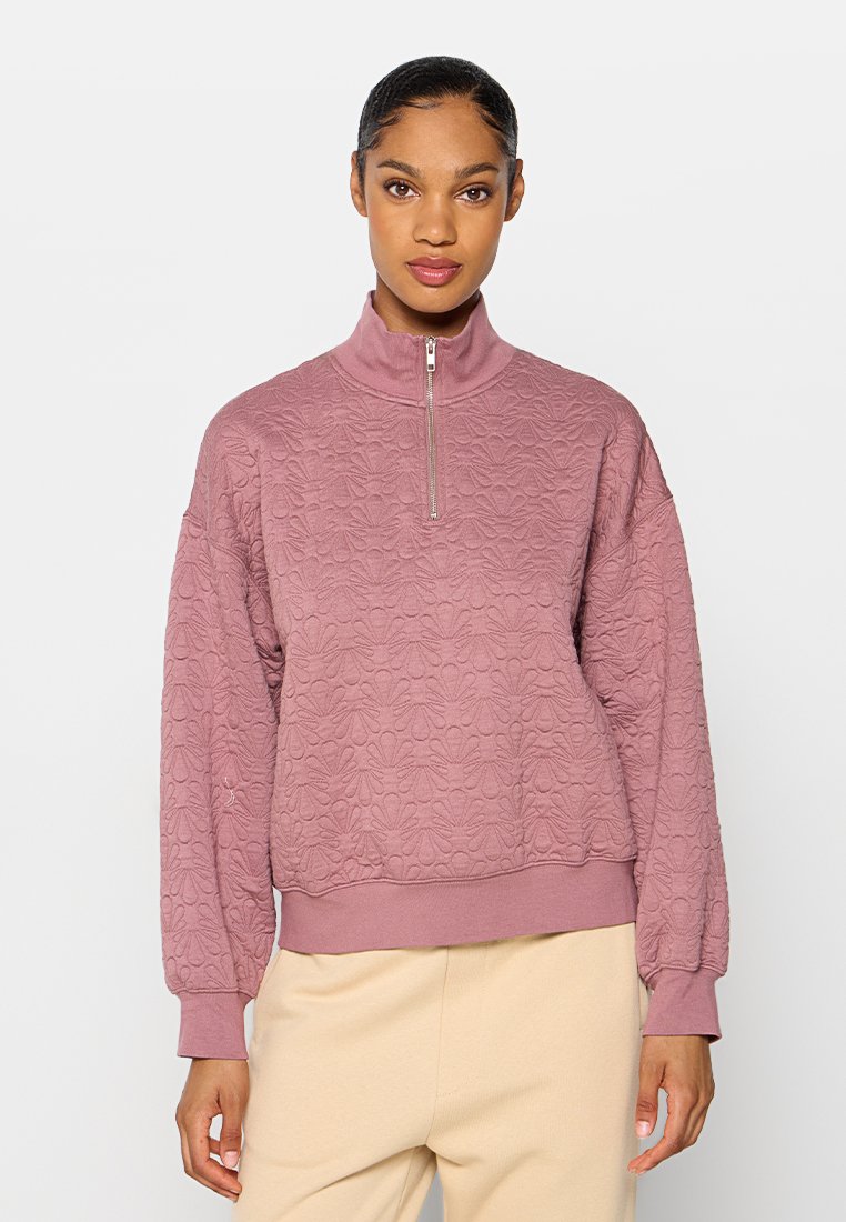 Texturiertes Sweatshirt mit Reißverschlusskragen in sanftem Rosa, das mit einem floralen Muster, gerippten Ärmelbündchen und einem lockeren Schnitt in der Taille ausgestattet ist.
