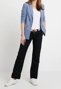 Lichtblauwe linnen blazer met dubbele knopen, witte t-shirt, zwarte broek met textuur, en witte sneakers met een gestreepte riem.