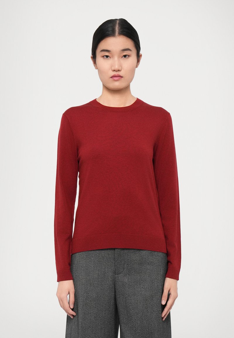 Maroon wool sweater with a round neck and long sleeves, featuring a ribbed hem and smooth texture, paired with gray wide-leg trousers.