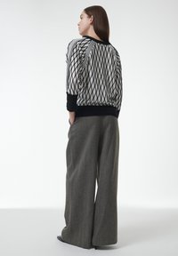 Schwarz-weiß gemusterter Pullover mit Rautenmuster und schwarzem Taillenbund, kombiniert mit hellgrauen, weit geschnittenen Hosen mit strukturierter Oberfläche.