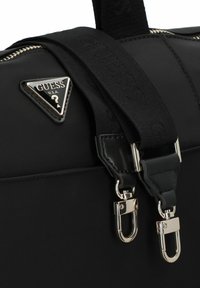 Borsa a mano nera in nylon con logo triangolare argentato, tracolla regolabile con branding in rilievo e dettagli hardware metallici.