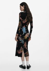 Schwarzes Langarmkleid mit bunten, komplexen Mustern, die verschiedene Meeresbewohner zeigen. Knielang mit einem seitlichen Schlitz; gerippte Textur.