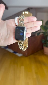 Schwarze Smartwatch mit einem silbernen Metallgehäuse und einem goldfarbenen Gliederarmband mit Strassakzenten, die die Uhrzeit 7:32 und das Datum anzeigt.