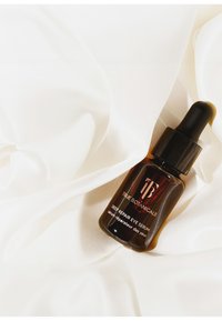 Bruine glazen druppelfles met een zwarte dop, gelabeld "True Botanicals Deep Repair Eye Serum," rustend op witte stof.