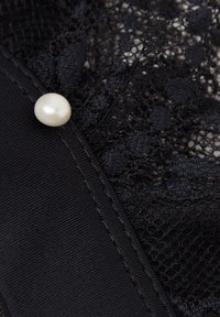 Czarna koronka z kwiatowymi wzorami ozdobiona pojedynczym białym guzikiem perłowym w pobliżu szytego brzegu.