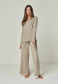 Beige knit lounge set featuring a v-neck long-sleeve top and wide-leg pants with a tie waist, designed with a ribbed texture and side slits.
