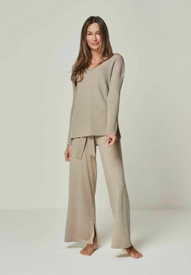 Beige knit lounge set featuring a v-neck long-sleeve top and wide-leg pants with a tie waist, designed with a ribbed texture and side slits.