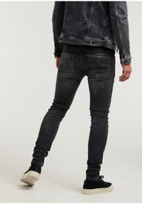 Černé džíny z denimové látky se slim fit střihem, s opotřebovanými detaily a dvojitými zadními kapsami, doplněné černou bundou a černými teniskami.