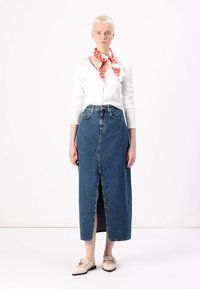 Denim maxi skjørt med en frontspalte, høy midje, blå farge og avslappet passform. Kombinert med en ribbestrikket hvit topp og et rødt mønstrete skjerf.