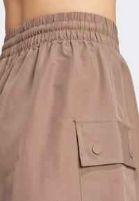 Beige shorts made of lightweight fabric, featuring an elastic waistband, side pocket with snap closure, and smooth texture.