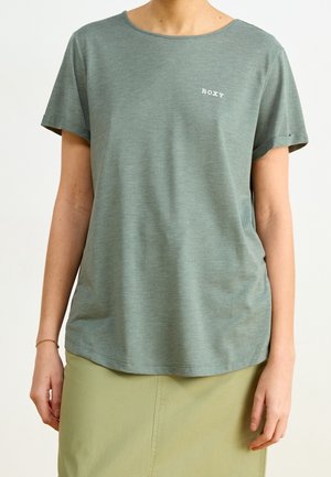 Person wearing a short-sleeve light green T-shirt with "ROXY" text on the chest and a light olive skirt against a plain background.